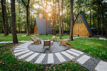 Modern wooden A-frame cabins in forest with outdoor seating and fire pit area, relaxation time