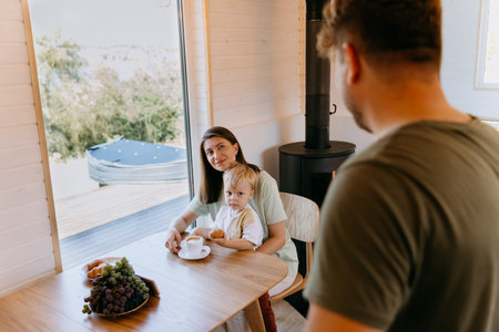 Mother and son enjoying breakfast with coffee and croissant while father watches in kitchen settingの写真素材