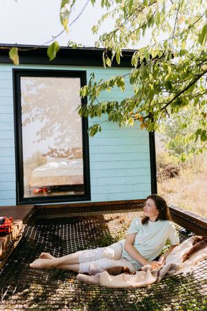 Relaxing outdoors, a woman enjoys a peaceful moment in a cozy, nature-filled setting by the houseの写真素材