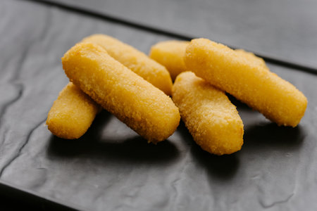 Crispy cheese sticks served on a black plate, perfect snack or appetizer for any occasionの写真素材