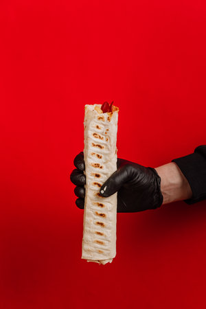 Hand holding wrap in paper against red background, fast food branding, marketing, and promotions