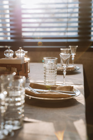 Elegant table setting with sunlight reflections creating a serene and warm dining experienceの写真素材