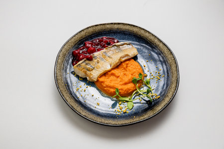 Baked fish fillet with mashed sweet potatoes and berry sauce, served with microgreens garnish