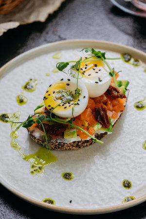 Gourmet toast with smoked salmon, boiled eggs, sun-dried tomatoes, and herbs served with black teaの写真素材