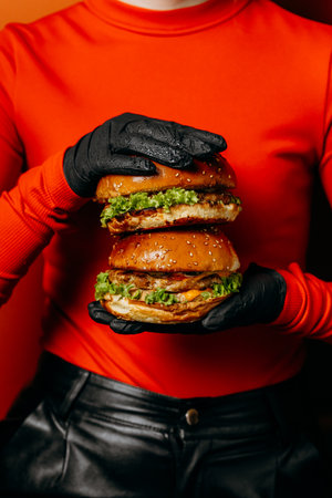Double cheeseburgers held with black gloves against bold red clothing, a striking food conceptの写真素材