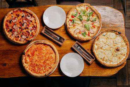 Assorted pizzas on a rustic wooden table, ready to serve with plates and cutleryの写真素材