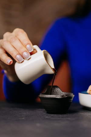 Close-up of a hand pouring soy sauce into a dipping bowl, perfect for sushi or Japanese cuisinの写真素材