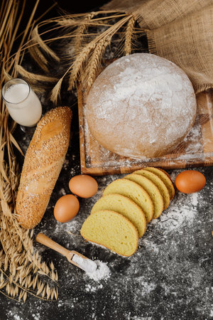 Rustic bread, eggs, milk, and wheat on a dark surface for natural baking inspiration