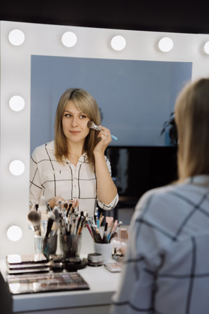 Applying makeup with a brush in front of a lighted mirror for a professional lookの写真素材