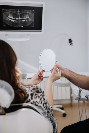 Dental patient with xray on screen, holding mirror during consultation for personalized treatmentの写真素材
