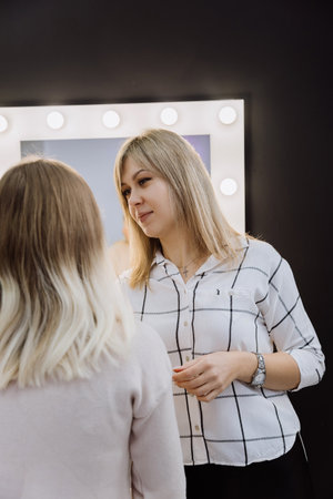 Professional makeup artist consulting a client in a studio setting with illuminated mirrorsの写真素材