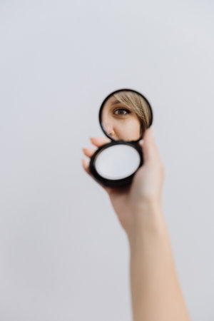 Focused eye reflection in a compact mirror held against a minimal backgroundの写真素材