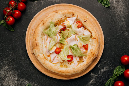 Gourmet salad pizza with lettuce, cherry tomatoes, turkey slices, and cheese on a wooden plateの写真素材