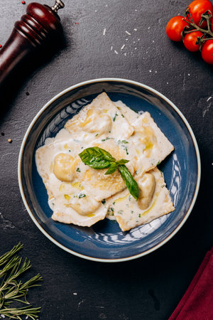 Creamy ravioli garnished with fresh basil leaves served on a blue plate, an Italian culinary delightの写真素材