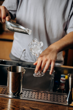 Bartender adding ice cubes to a cocktail glass, setting the stage for a perfectly crafted drinkの写真素材