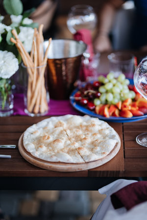 Delicious flatbread served alongside fresh fruit and breadsticks on a beautifully set dining tableの写真素材