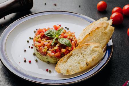 Guacamole tartare with fresh vegetables, basil garnish, and crispy baguette slices on a white plateの写真素材