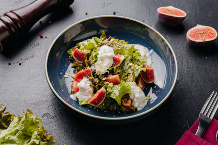 Fresh fig and burrata salad with leafy greens, almonds, and creamy dressing in a rustic blue bowlの写真素材