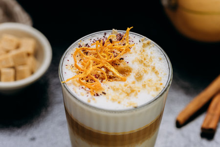 Gourmet layered latte with whipped foam, orange zest, and spices, served on a rustic dark surface