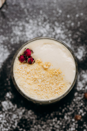 Creamy latte with coconut flakes and dried rose garnish, served in a glass with a velvety frothy topの写真素材