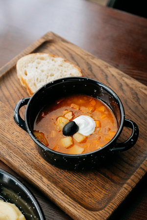 Hot bowl of rustic solyanka soup with sour cream, black olive, and fresh bread sliceの写真素材