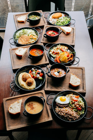 Assorted restaurant-style meals served in black bowls on wooden trays, top viewの写真素材