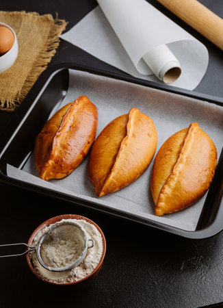 Freshly baked pies in baking tray, traditional homemade pastry with golden crust. Ukrainian piroshki