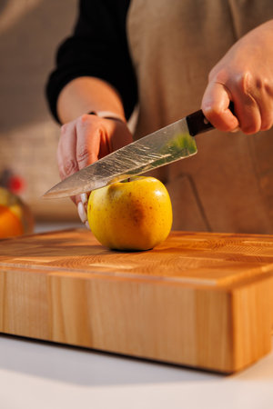 Woman slicing yellow apple on wooden cutting board in warm home kitchen