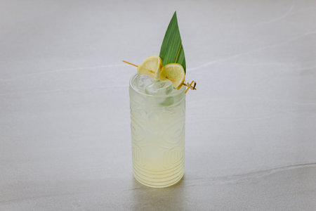 Refreshing tropical cocktail with lemon slices and ice in a tiki glass on gray background