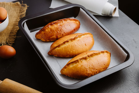 Golden homemade pies in baking tray, rustic kitchen scene with rolling pin and eggsの写真素材