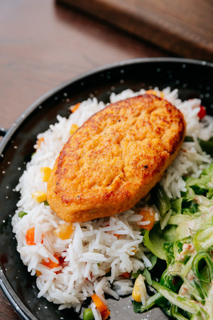 Close-up of grilled cutlet on vegetable rice with fresh green salad on black plateの写真素材