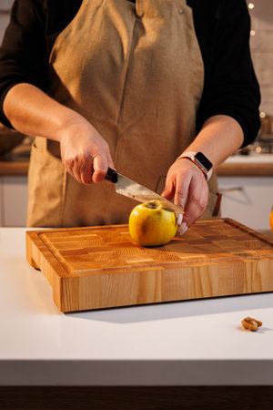Woman slicing a yellow apple on a wooden board in warm kitchen lightの写真素材