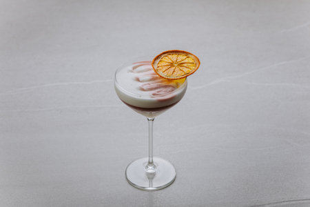 Elegant layered cocktail with citrus garnish and foam in a coupe glass on grey backgroundの写真素材