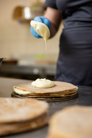 Pastry chef spreading cream on cake layer in professional bakery kitchen, close-upの写真素材