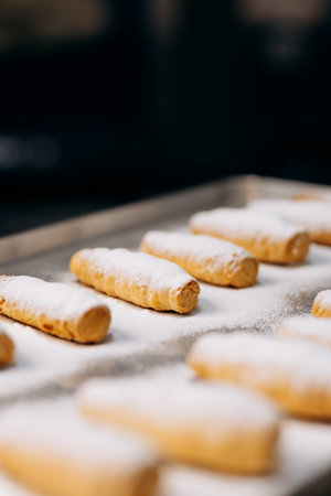 Freshly baked cream rolls sprinkled with powdered sugar on a metal tray in bakeryの写真素材