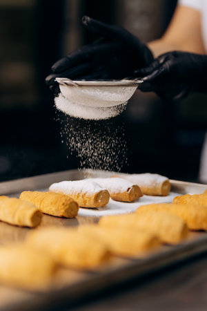Chef dusting pastries with powdered sugar on tray in modern bakery kitchenの写真素材