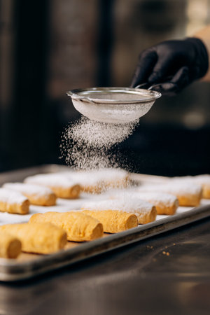 Chef dusting pastries with powdered sugar on tray in modern bakery kitchenの写真素材