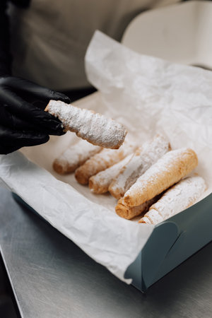 Freshly baked cream horns in powdered sugar held in hand over pastry boxの写真素材
