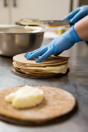 Chef assembling layered cake with cream in professional kitchen, close-up on hands and processの写真素材