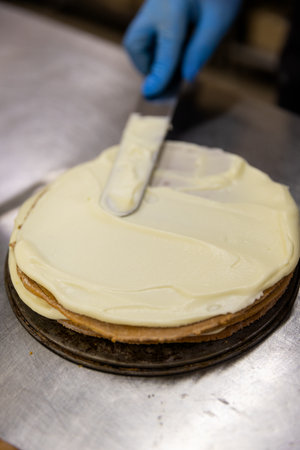 Spreading creamy custard on a cake layer in a professional bakery kitchenの写真素材