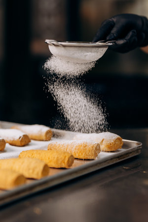 Chef dusting pastries with powdered sugar on tray in modern bakery kitchenの写真素材