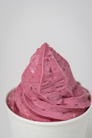 Vibrant pink berry soft serve in white cup, close-up shot on light background