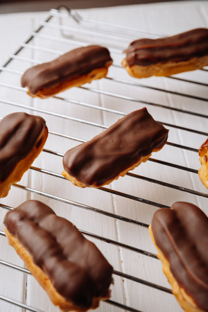 Freshly baked chocolate eclairs cooling on a rack in natural warm light