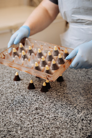 Handmade chocolate candies being unmolded at confectionery factory by chocolatier in gloves