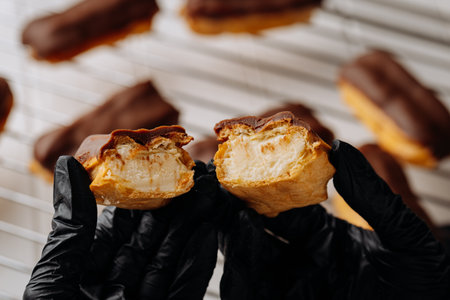 Close up of chocolate eclair with creamy filling held in gloved hands on cooling rack