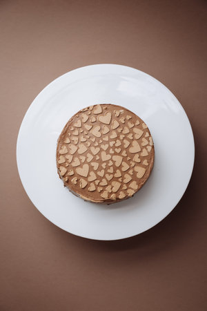 Chocolate cake with heart shaped decor on stand, minimal brown background