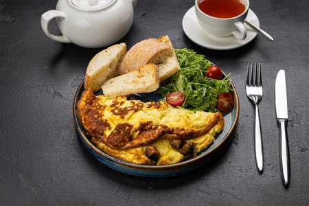 Healthy breakfast with omelet, ciabatta, salad and tea on dark stone backgroundの写真素材
