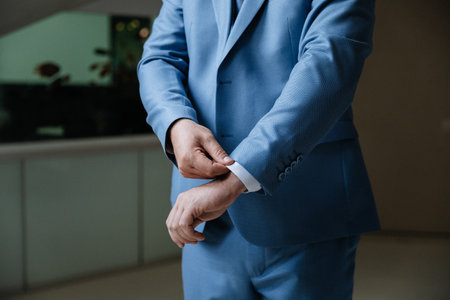 Man adjusting sleeve of blue suit, close-up, elegant formal style, indoors