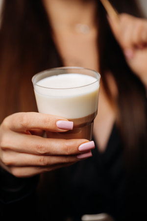 Layered dessert with creamy milk mousse and chocolate in a glass, held by womans hand