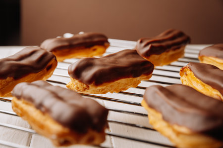 Freshly baked chocolate eclairs cooling on a rack in natural warm light